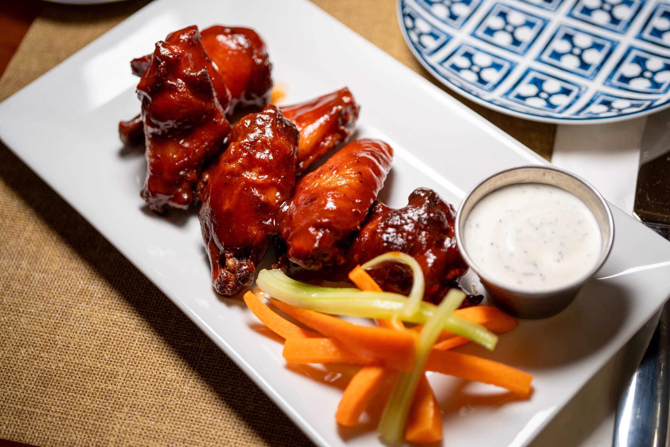 BBQ chicken wings with celery, carrot sticks, and ranch dip on a white plate, perfect for appetizers or game day snacks.