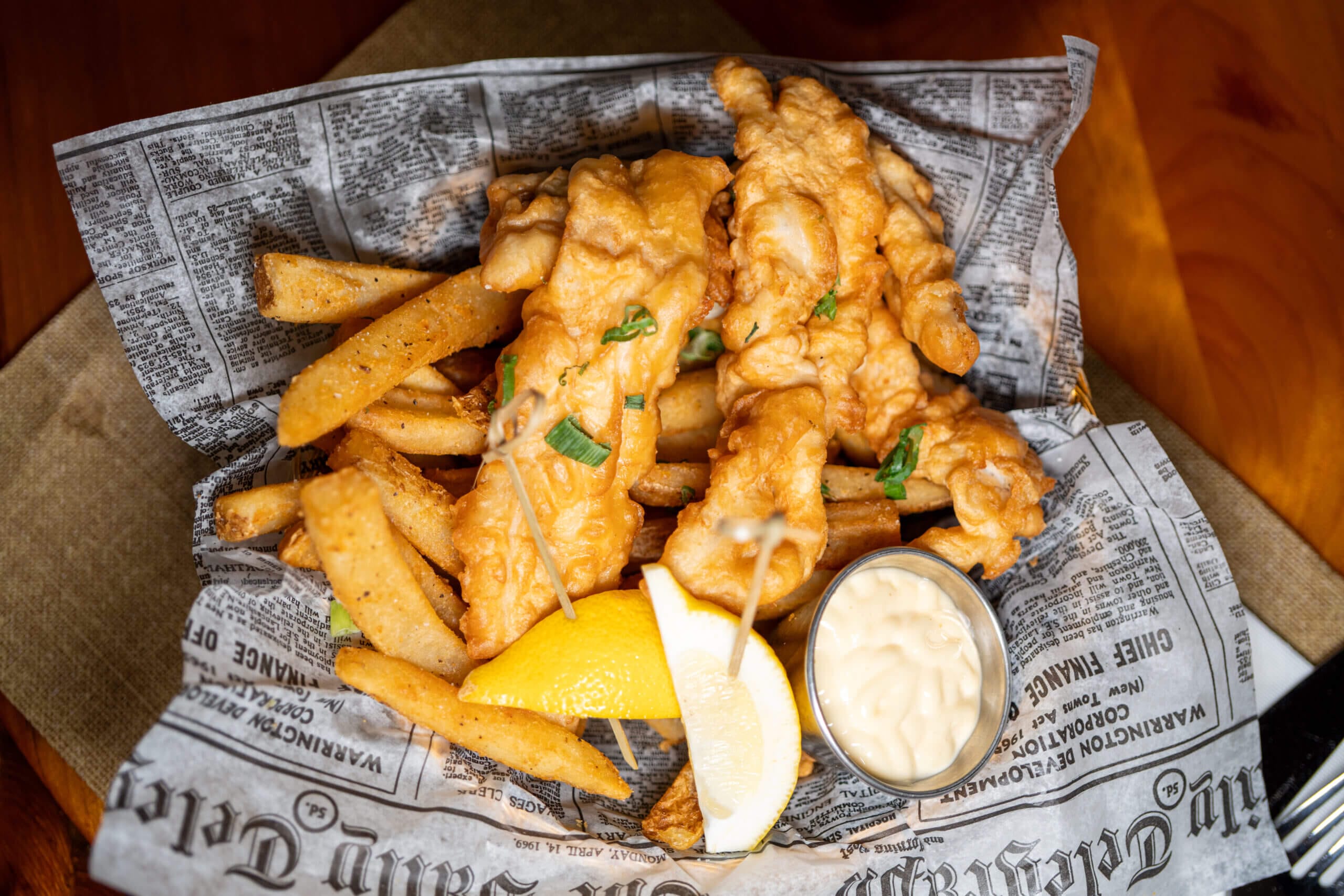 Crispy fish and chips with lemon and tartar sauce on newspaper-style paper.
